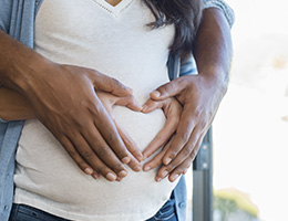   Two pairs of hands overlap on a pregnant stomach, forming a heart