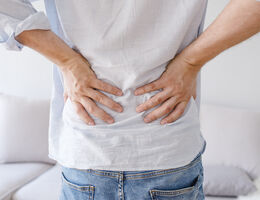 A person holds their hands to their lower back as if in pain. 