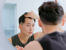 A young man examines his hairline in the mirror.